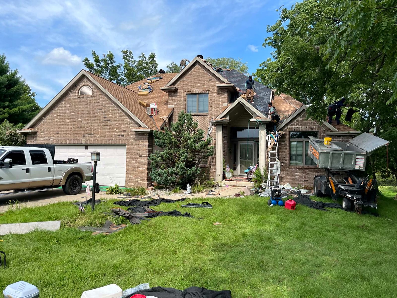 The Forge Roofing crew mid tear off on a brick two story home, underlayment down and a dump trailer in the drive